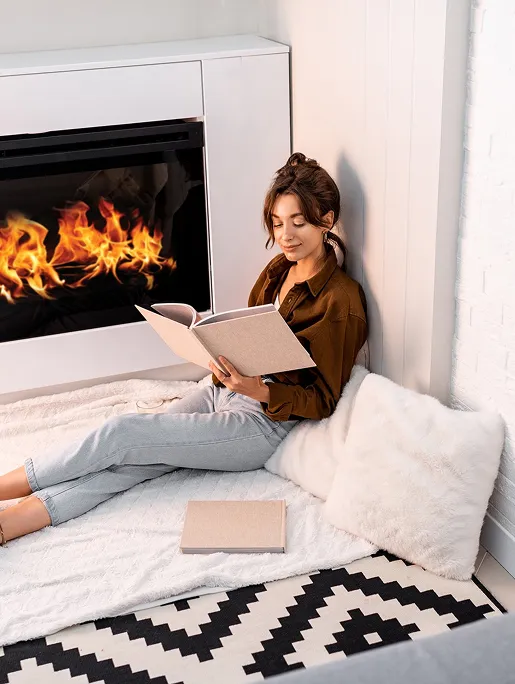 Femme lit un livre sur le sol près d'une cheminée allumée à Sainte Gemme la Plaine près de Luçon en Vendée 85